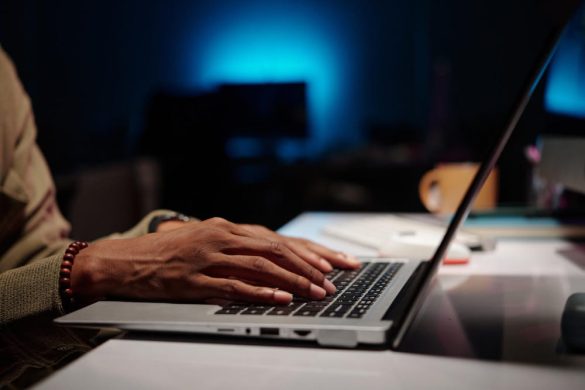 Mains d'un entrepreneur tapant sur le clavier d'un ordinateur portable le soir pour profiter d'un nom de domaine pas cher pour lancer votre projet.