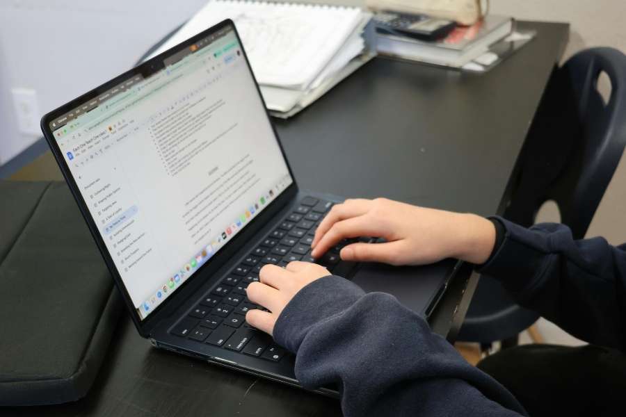 Un enfant tape sur un laptop noir ouvert sur un bureau scolaire, parfait exemple des laptops abordables adaptés aux étudiants.
