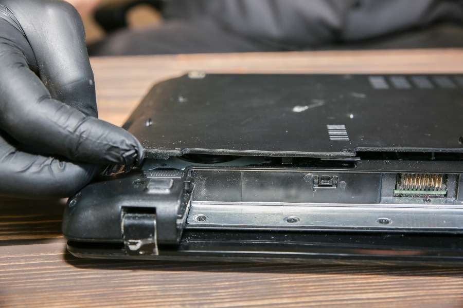 Technicien avec des gants noirs retirant la batterie de son laptop pour une réparation ou un remplacement.