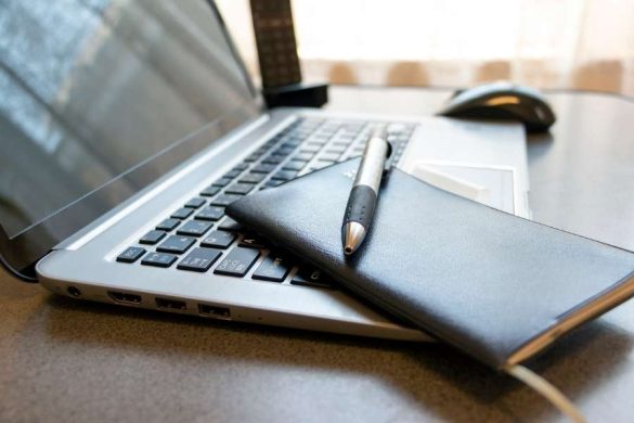 Un laptop argenté ouvert sur un bureau avec un carnet noir et un stylo posés dessus, représentant les laptops abordables pour professionnels.