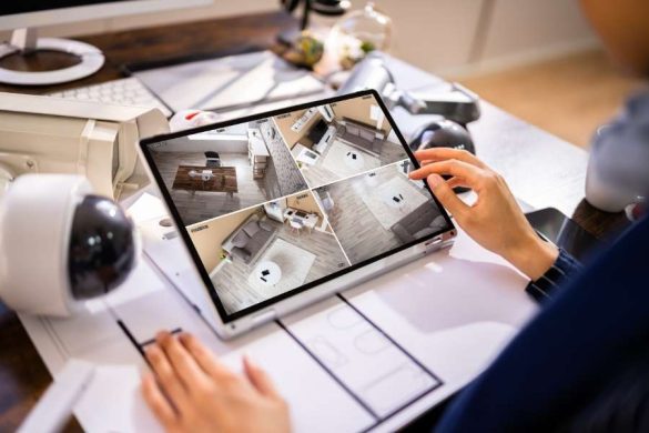 Une personne utilise une tablette tactile posée sur un bureau pour surveiller les flux vidéo de quatre pièces différentes dans le cadre d'un Ajax systems avis.