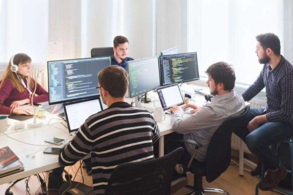 Une équipe de professionnels travaille sur plusieurs ordinateurs et écrans affichant des lignes de code dans un bureau.