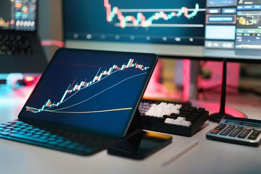 Écran de tablette et moniteurs affichant un graphique crypto pour le suivi des marchés.